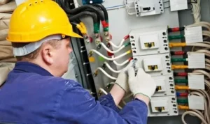 a commercial electrician in a yellow hard hat repairing an industrial electrical panel with colorful wiring, emphasizing commercial electrical services