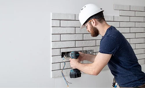 A residential electrician in Highland Park, CA installing new electrical wiring for electrical outlets in a residential setting, wearing a hard hat and using a power drill, emphasizing safety and professional service